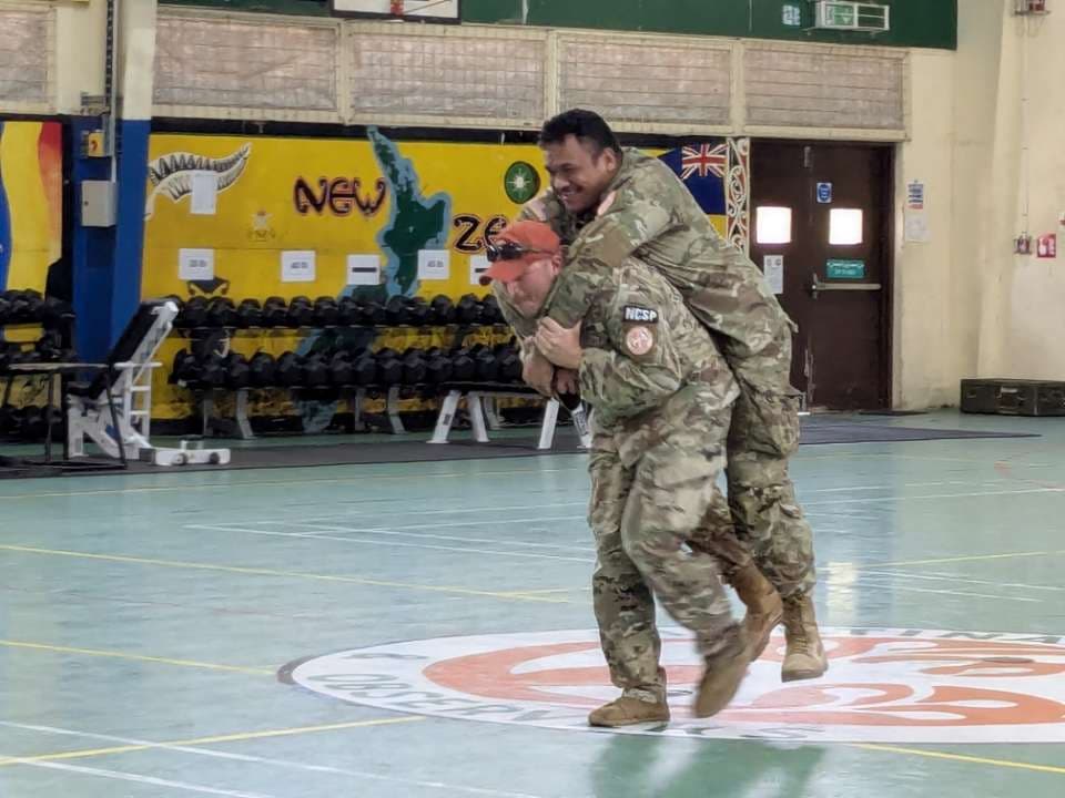 Two men embrace at an indoor event; one is wearing camouflage clothing.